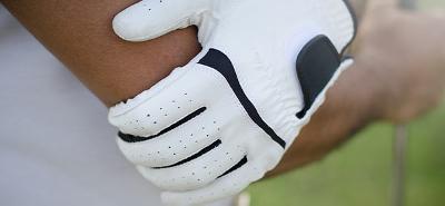 A golfer wearing a golfing glove holding his elbow